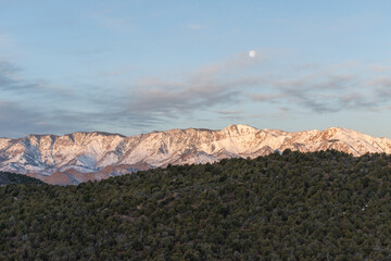 Scenic view of snow-covered mountains at Kolob Canyons in Zion National Park, Utah. A serene winter landscape under a clear sky with a visible moon, showcasing natural beauty and tranquility - USA