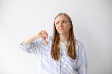 Portrait of blonde woman in shirt showing thumbs down, dislike something, looking disappointed,...