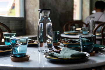 A beautiful round table set with blue and green plates and glasses, and a clear jug of water.