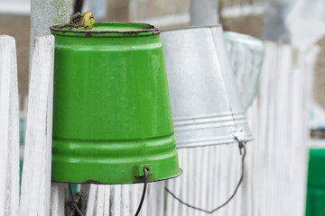 Empty metal buckets hang on the fence. Dishes for water in a country house.