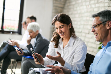 Happy business colleagues using cell phone while waiting for a job interview in the office