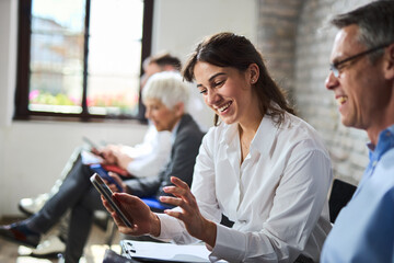 Happy business colleagues using cell phone while waiting for a job interview in the office