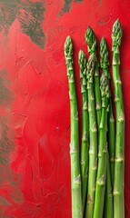 A row of fresh asparagus spears against a red textured background. Ideal for culinary blogs, recipe cards, or health food advertisements.