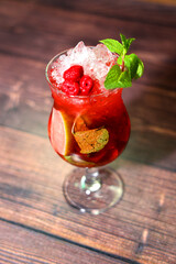 Refreshing raspberry drink with ice and mint in a tall glass on a wooden background