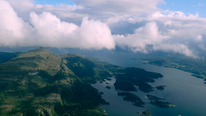 Aerial view through the clouds to the sea bay with coastal hills. Top view from the clouds to the Norwegian fjords