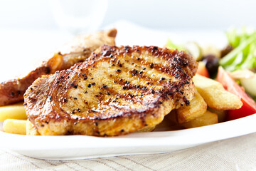 Grilled Steaks with french fries and fresh salad. Bright wooden background.	