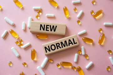 New normal symbol. Wooden blocks with words New normal. Beautiful pink background with pills....