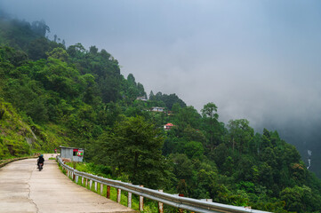 Concrete road passing through Himalayan mountains and lush green forest. Scenic natural beauty of...