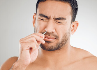 Obraz premium Man, nose and pain for hair removal, tweezers and dermatology for skincare in studio in morning. Asian male person, wellness and maintenance for face with epilation and tools by white background