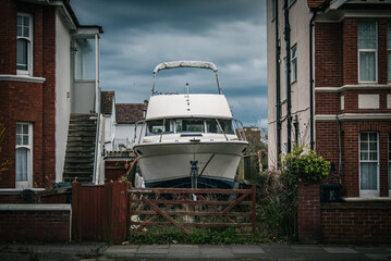 Small yacht, boat parked up in town between two buildings before being transported, Brighton, East Sussex, UK