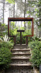 Scenic Outdoor Photo Spot with Wooden Frame Amidst Lush Greenery and Forest Background, Perfect for Couples to Relax and Enjoy Nature