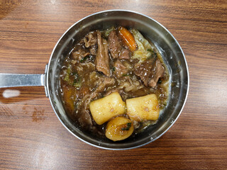 Close Up of Korean Galbi Jjim (Braised Beef Short Ribs) and korean tteokbokki in a Stainless Steel Pan on a Wooden Table