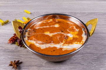 a traditional copper bowl of Indian butter chicken with spices scattered