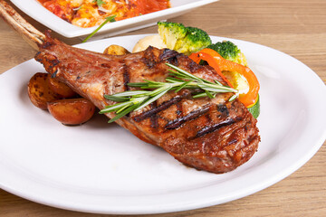 a dinner plate filled with a grilled veal chop and assorted vegetables in a restaurant setting