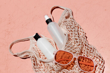 Mockup of skincare bottles in mesh market tote with orange-colored sunglasses in direct sunlight on coral background