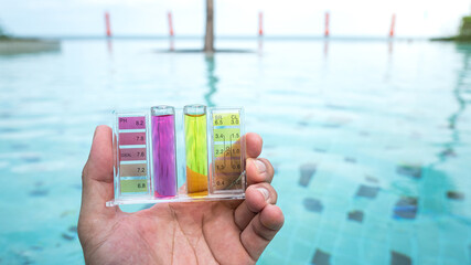 A swimming pool service worker is holding a water tester kit which is using for measuring pH value and Chloring concentration. With background of the blue water swimming pool.