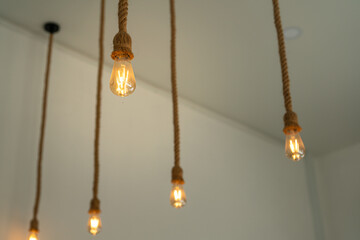 Rope ceiling lighting bulb glowing in orange warmlight shade, which is installed at living room for cozy design. Interior decoration object photo, close-up and selective focus.