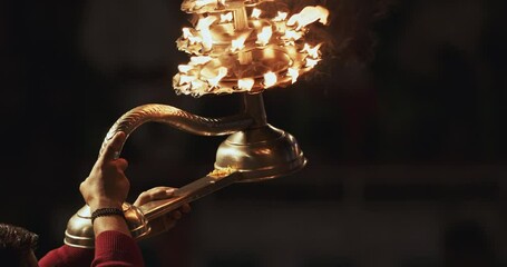 Varanasi, India. Man makes movements with a candle holder with lit candles on the Ganga Maha Aarti ceremony begins. Brahman priest wearing red and yellow dress doing traditional ganga aarti at ghat