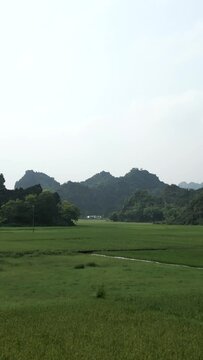 Drone flying over the green crop fields among the forested mountains of Hanoi Vietnam on a gray day