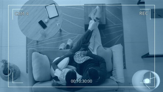 Directly above security camera shot of biracial loving spouses sitting together on couch with popcorn when watching TV