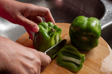 Concept of taking or grabbing food with hands, feminine Mexican hands. Cutting green peppers with a kitchen knife on a wooden chopping board using both hands, horizontal side view image.