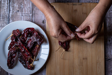 Concept of taking or grabbing food with hands, feminine Mexican hands. chile seco guajillo on a wooden cuuting board and on a white plate, flat lay horizontal top view