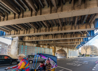 Under the Southwark Street railway bridge with an older man driving a three wheeled motorbike taxi with a father and son sightseeing around London, England, UK.