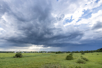 Fototapeta premium A wide shot of a field with lush green grass, surrounded by a dark, stormy sky with patches of light blue peeking through.
