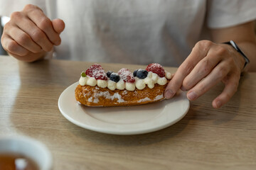 A close-up shot of a persons hand reaching for a delicious eclair topped with fresh strawberries...