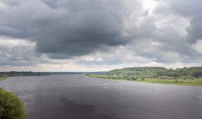 A panoramic view of a river winding through a lush green landscape, with a dramatic sky filled with dark, ominous clouds.