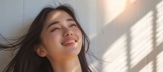 Beautiful young Asian woman smiling and happily with long hair blowing in the wind, looking up at sunlight shining