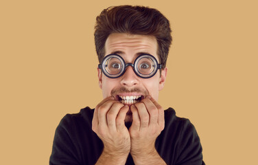 Portrait of a funny stressed and nervous nerdy student. Young man in round glasses biting his fingers and looking at the camera with a very worried, scared face expression