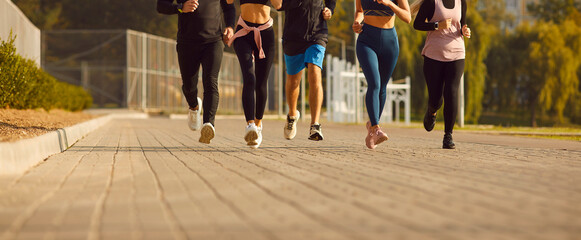 Legs of team of sporty people men and women running together in park having sport workout outdoors....