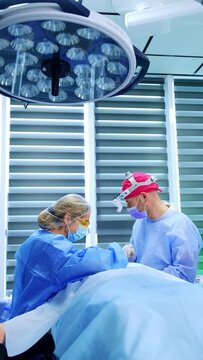 Two medics stand at the operational table in modern hospital. Male doctor and assisting nurse perform surgery. Vertical video.
