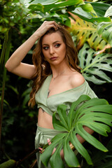Portrait of a young woman with blond hair standing under a big banana leaf and looking at camera.