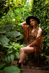 Cowboy girl in black hat and leopard dress. In the background there are many trees and a tropical forest