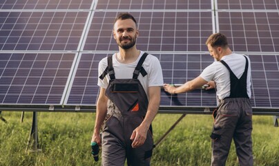 Two skilled workers or craftsmen wearing working gray uniforms, technicians are installing solar panels on a solar farm for clean energy and electricity supply