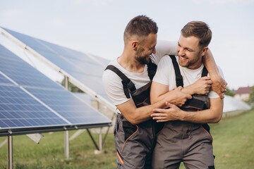 Two happy bearded gay in work uniforms joying and flirting with each other hugging on the background of solar panels