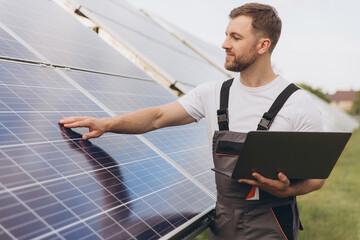 Engineer or construction worker bearded man uses laptop to check solar panel system status. Cell...