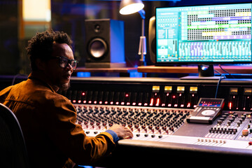 Sound designer working on control desk in professional studio, using faders and switchers to edit...