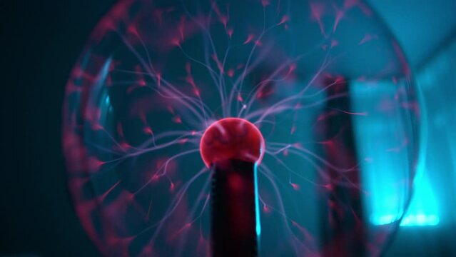 Plasma tongues in lamp based on operation of tesla coil. charged particles inside plasma globe creating gas light beams inside. Closeup of lasers moving from red plasma ball. Shooting in slow motion.