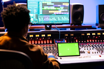 African american audio engineer looks at greenscreen on device and digital editing software on...