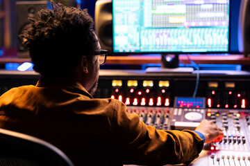 Sound engineer uses mixing console and handling panel board buttons, pushing sliders in control...