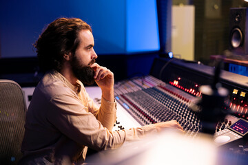 Music producer editing tracks with mixing console and faders, operating control desk to remove...
