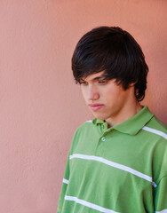 single young man with long hair and green polo shirt against a simple background outdoors