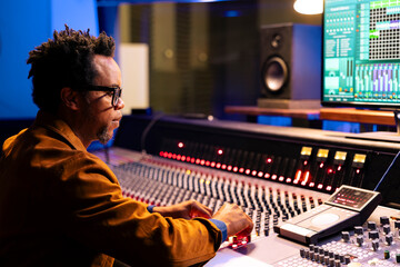 African american sound technician using audio console with moving faders and colored meters for...