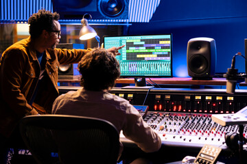 Team of artists collaborating on processing recorded files with audio software, pushing faders to...
