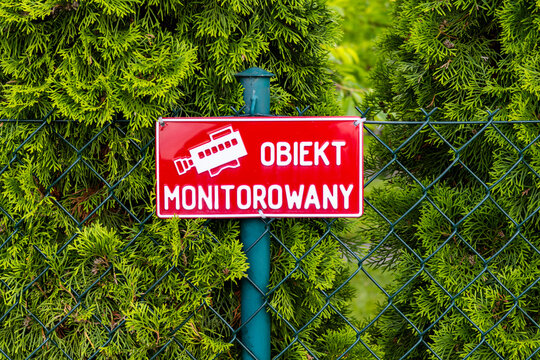 A sign indicating the area under video surveillance against the background of a wire fence and green bushes.
