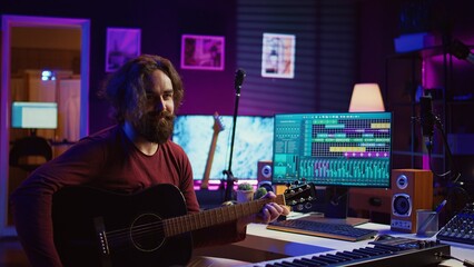 Young man songwriter playing guitar and creating music using equalizer program. Musician recording song in home studio, engineer mixing and mastering pop rock tracks. Camera B.