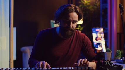 Obraz premium Artist teaching online piano lessons from his home studio, recording tutorial and playing midi controller synthesizer. Instructor explaining electronic keyboard notes, music industry. Camera A.